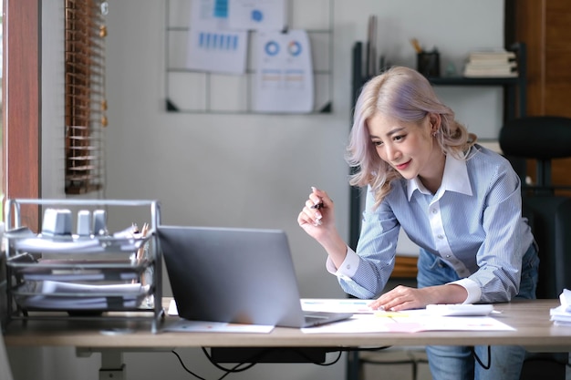 La joven empresaria asiática está feliz de trabajar en la oficina moderna usando una tableta