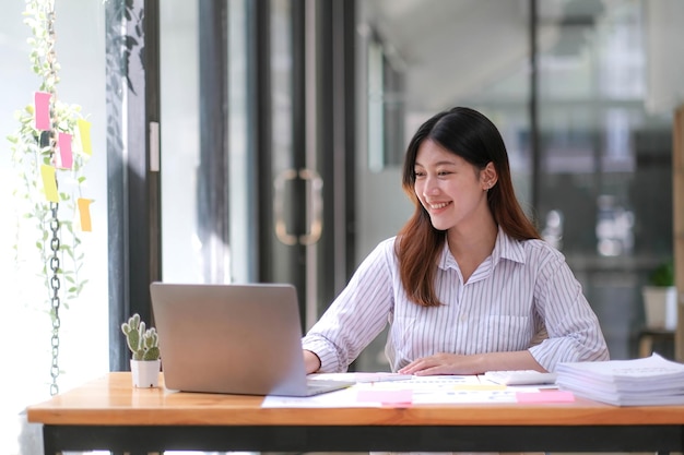 La joven empresaria asiática está feliz de trabajar en la oficina moderna usando una tableta