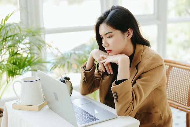 Una joven empresaria asiática estresada está usando una laptop para trabajar en línea Pequeñas empresarias cansadas