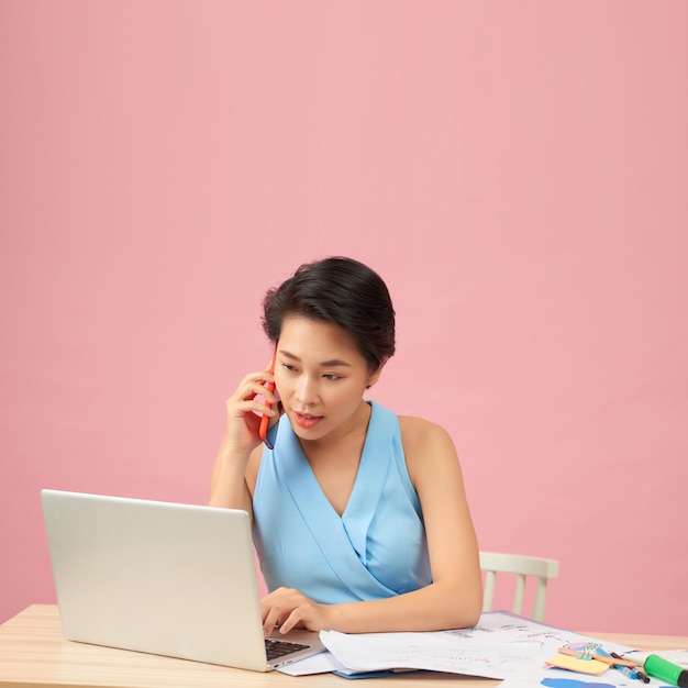 Joven empresaria asiática hablando por teléfono y trabajando en una laptop