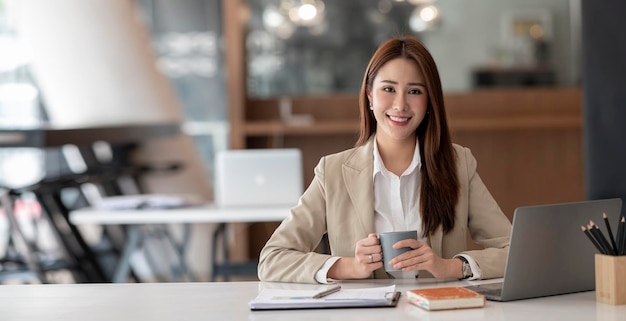 Joven empresaria asiática hermosa encantadora sonriendo y hablando por teléfono móvil sentada en la oficina