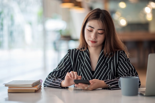 Joven empresaria asiática hermosa encantadora sonriendo y usando el teléfono móvil en la oficina