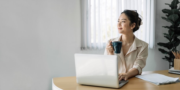 Joven empresaria asiática sonriendo sostiene la taza en la oficina