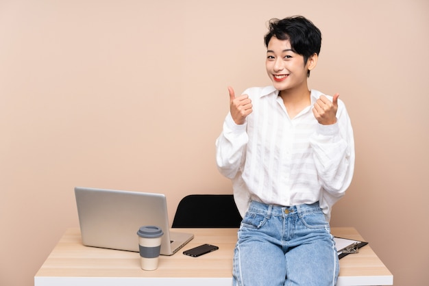 Joven empresaria asiática en su lugar de trabajo dando un gesto de aprobación