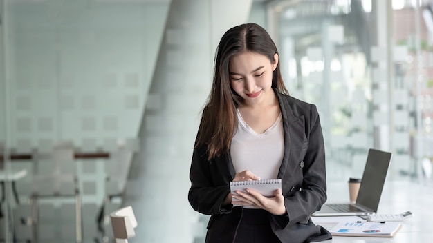 una joven empresaria asiática tomando notas en la oficina.