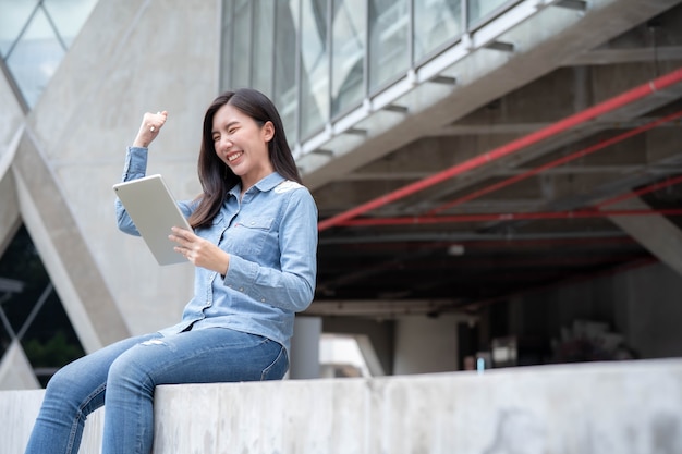 Joven empresaria asiática trabajando en línea en tableta y regocijo