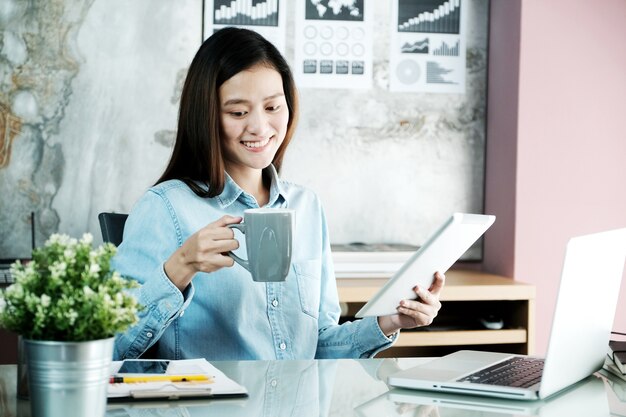 Joven empresaria asiática trabajando con tableta y computadora portátil con cara sonriente