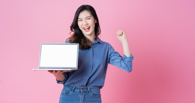 Joven empresaria asiática usando laptop sobre fondo rosa