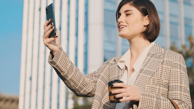 Joven empresaria atractiva haciendo videollamadas con colegas tomando café para salir al aire libre. Siempre en contacto