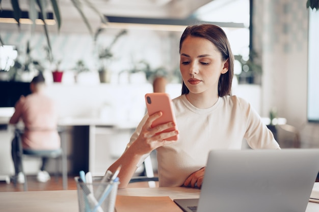 Joven empresaria atractiva con su teléfono inteligente en la oficina