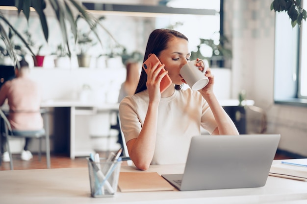 Joven empresaria atractiva con su teléfono inteligente en la oficina