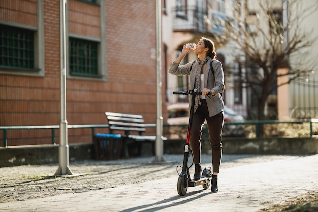 Una joven empresaria bebiendo café durante el trabajo con un scooter eléctrico.