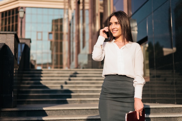 Joven empresaria en una blusa y una falda está hablando por teléfono.