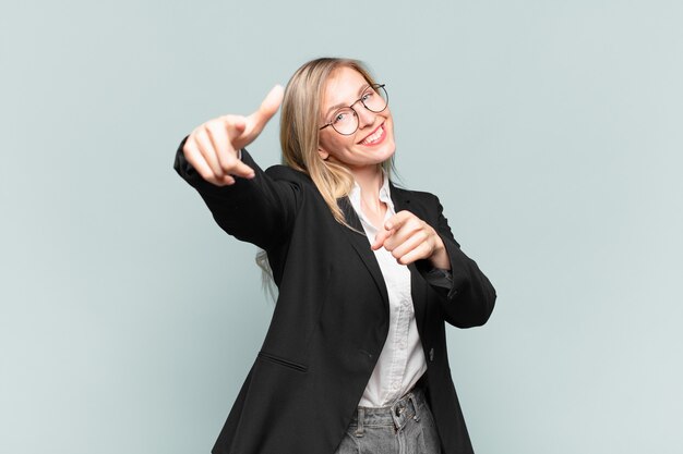 Joven empresaria bonita que se siente feliz y confiada, apuntando a la cámara con ambas manos y riendo, eligiéndote