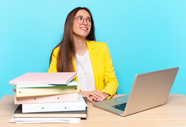 Joven empresaria bonita que se siente feliz, orgullosa y esperanzada, preguntándose o pensando, mirando hacia arriba para copiar el espacio con los brazos cruzados