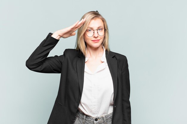 Joven empresaria bonita saludando a la cámara con un saludo militar en un acto de honor y patriotismo, mostrando respeto