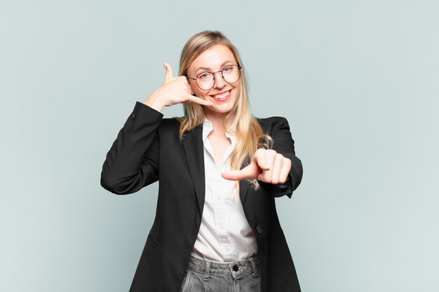 Joven empresaria bonita sonriendo alegremente y apuntando a la cámara mientras hace una llamada, gesto más tarde, hablando por teléfono