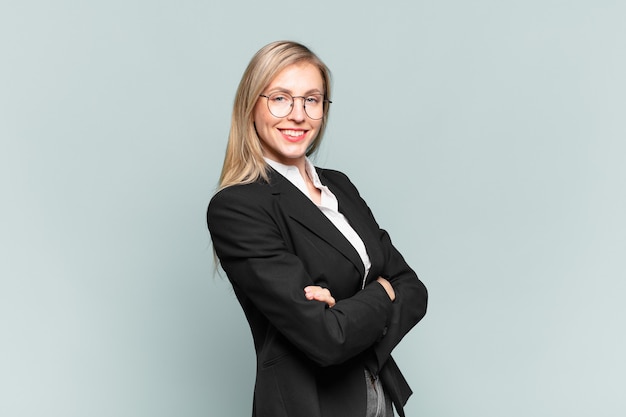 Joven empresaria bonita sonriendo a la cámara con los brazos cruzados y una expresión feliz, confiada y satisfecha, vista lateral