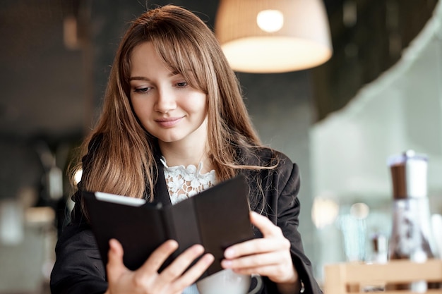 Joven empresaria en un café leyendo un libro electrónico y tomando café