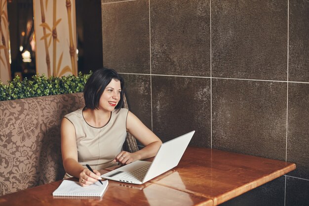 Joven empresaria caucásica sonriente con portátil y portátil. Mujer en cafe