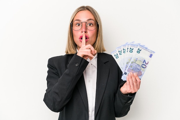 Joven empresaria caucásica sosteniendo billetes aislados de fondo blanco guardando un secreto o pidiendo silencio