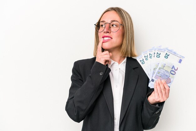 Joven empresaria caucásica sosteniendo billetes aislados de fondo blanco relajado pensando en algo mirando un espacio de copia