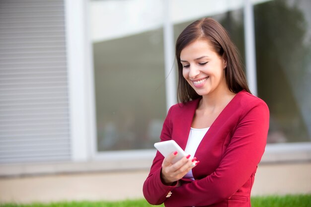 Joven empresaria en chaqueta roja con teléfono móvil al aire libre