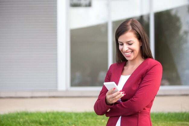 Joven empresaria en chaqueta roja con teléfono móvil al aire libre