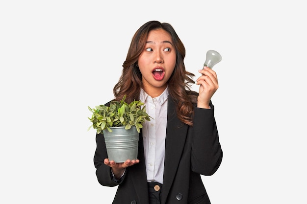 Una joven empresaria china sostiene una bombilla y una planta que encarna sus ideas innovadoras