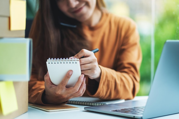 Joven empresaria confirmando y anotando pedidos del cliente en el teléfono para compras en línea y concepto de entrega