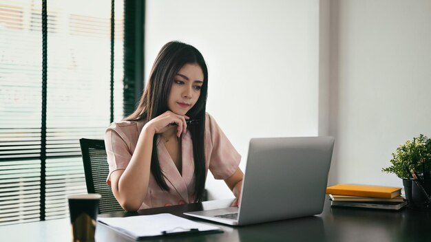 Joven empresaria enfocada analizando datos financieros en su computadora portátil