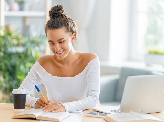 Joven empresaria enfocada que estudia en línea, mira seminarios web, podcast en una laptop, toma notas, se sienta en el escritorio. Concepto de aprendizaje electrónico.