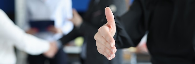 Joven empresaria estirando su mano para apretón de manos en el fondo de primer plano de colegas