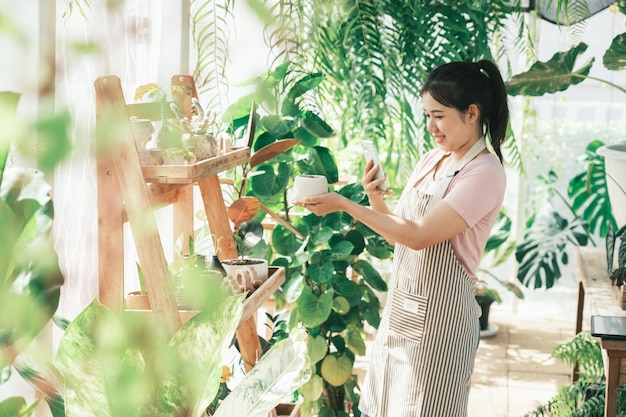 Joven empresaria florista sonriente tomando fotos de plantas en macetas por teléfono para el comprador El concepto de ventas en línea de plantas