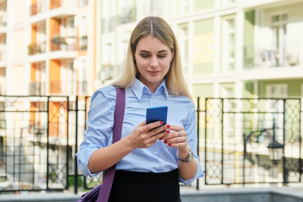 Joven empresaria con fondo de edificio de oficinas de calle de teléfono inteligente