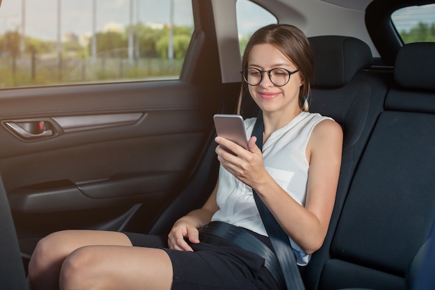 Joven empresaria con gadget sentado en coche moderno