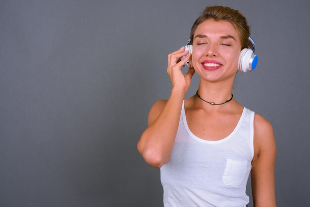 Joven empresaria hermosa con cabello rubio escuchando música en gris