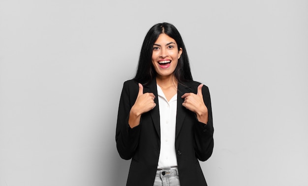 Joven empresaria hispana que se siente feliz, sorprendida y orgullosa, apuntando a sí misma con una mirada emocionada y asombrada