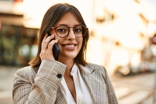 Joven empresaria hispana sonriendo feliz hablando por el teléfono inteligente en la ciudad.