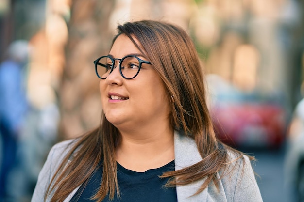 Joven empresaria hispana de talla grande sonriendo feliz de pie en la ciudad