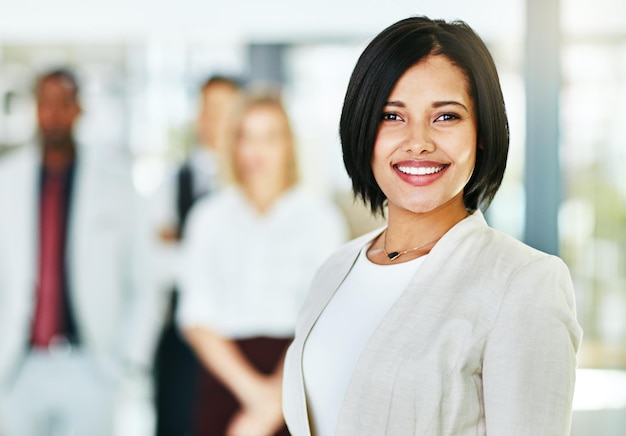 Foto joven empresaria inteligente y sonriente con un equipo diverso en el trabajo listo para lograr el éxito ejecutiva profesional segura de sí misma de pie en una oficina moderna con sus colegas en el fondo