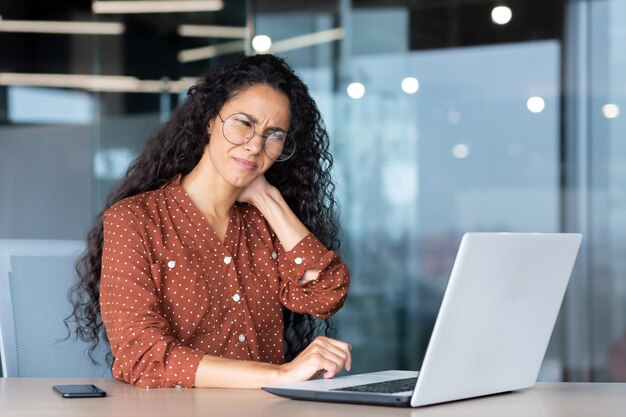 Una joven empresaria latinoamericana cansada, independiente, se sienta en el escritorio de la oficina y trabaja horas extras