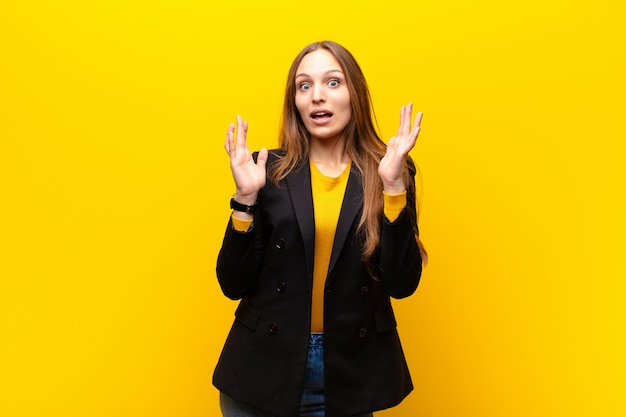 Joven empresaria linda que parece sorprendida y asombrada, con la boca abierta de sorpresa al darse cuenta de algo increíble contra la pared naranja