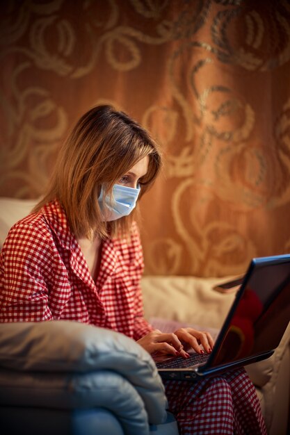 Joven empresaria en una máscara protectora médica trabaja desde su casa en la computadora durante el autoaislamiento y la cuarentena. Brote de coronavirus del virus, epidemia de gripe y novela covid ncov. Quedarse en casa.