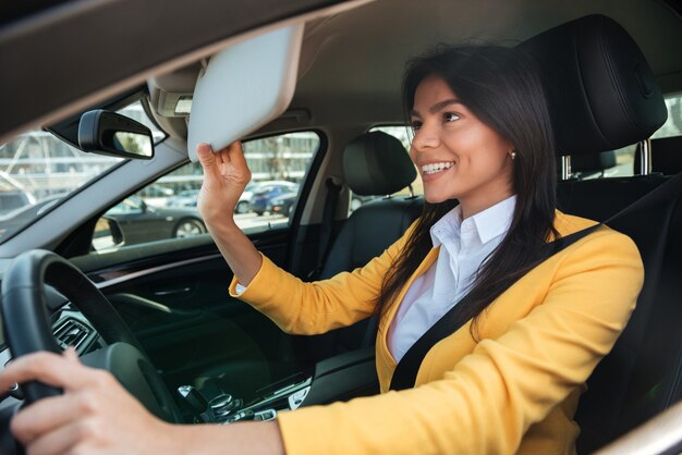 Joven empresaria mirando en el espejo mientras conduce un auto