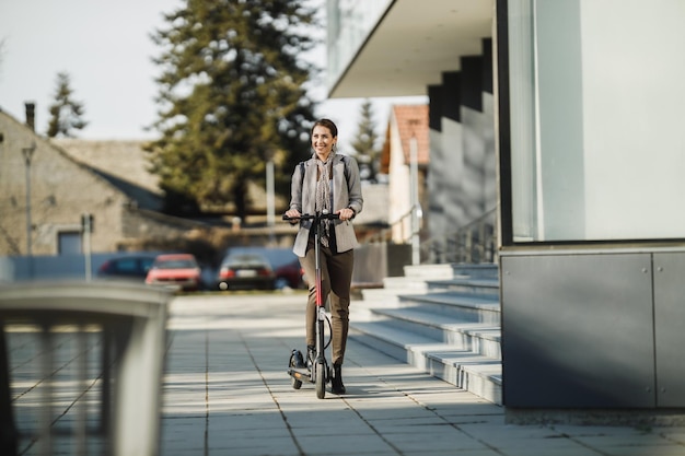 Una joven empresaria montando un scooter eléctrico de camino al trabajo.