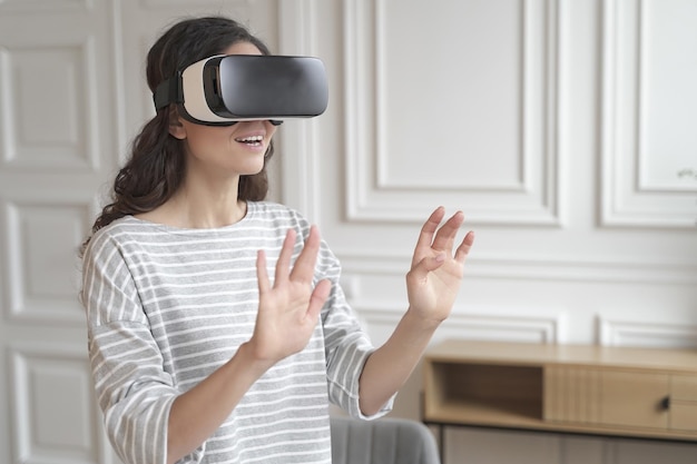 Joven empresaria morena impresionada interactuando con la realidad virtual con gafas de realidad virtual