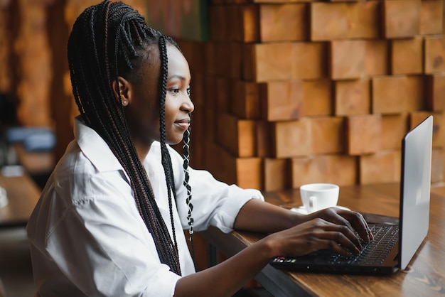 Joven empresaria o estudiante afroamericana enfocada mirando una laptop mujer negra seria trabajando o estudiando con una computadora investigando o preparándose para un examen en línea