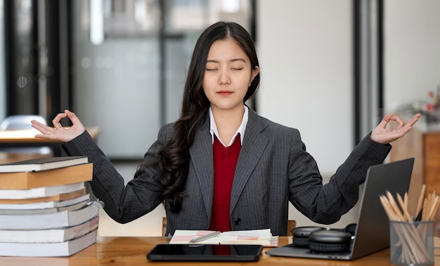 Joven empresaria o estudiante practicando ejercicios de yoga de respiración en la meditación de la oficina del lugar de trabajo