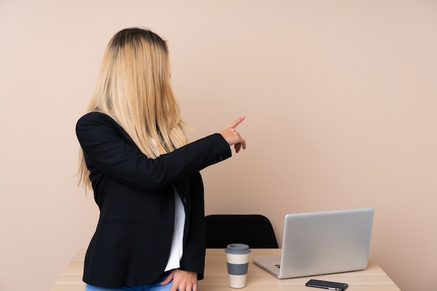 Foto joven empresaria en una oficina apuntando hacia atrás con el dedo índice